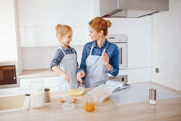 bella madre in una camicia blu e grembiule sta preparando la cena a casa in cucina