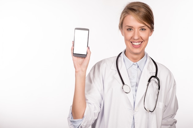 Bella medico femminile sorridente e mostrando un telefono astuto in bianco