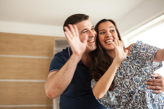 Bella moglie e marito che chiamano i loro genitori per mostrargli il nuovo appartamento che hanno. Coppia felice che saluta la telecamera