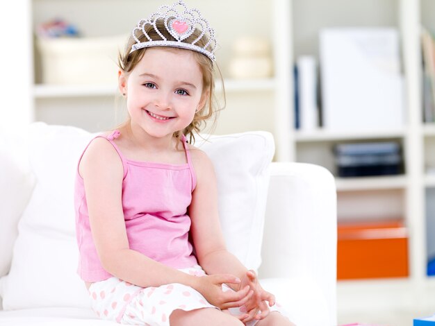 Bella piccola graziosa principessa in corona con il sorriso seduto sul divano