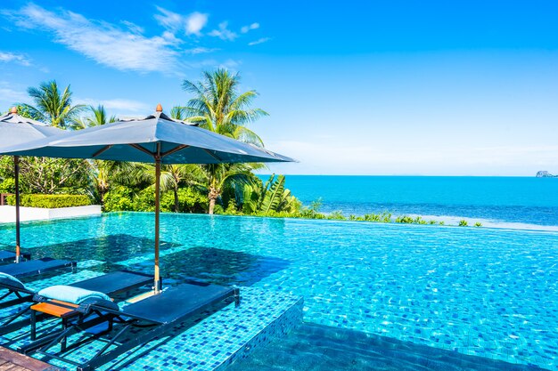 Bella piscina all'aperto di lusso nella località di soggiorno dell'hotel con l'oceano del mare intorno all'albero del cocco e nuvola bianca su cielo blu