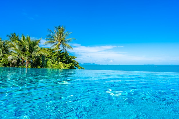 Bella piscina all'aperto di lusso nella località di soggiorno dell'hotel con l'oceano del mare intorno all'albero del cocco e nuvola bianca su cielo blu