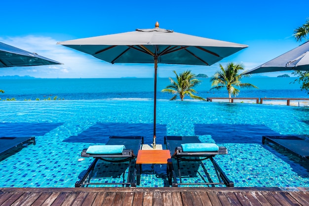 Bella piscina all'aperto di lusso nella località di soggiorno dell'hotel con l'oceano del mare intorno all'albero del cocco e nuvola bianca su cielo blu