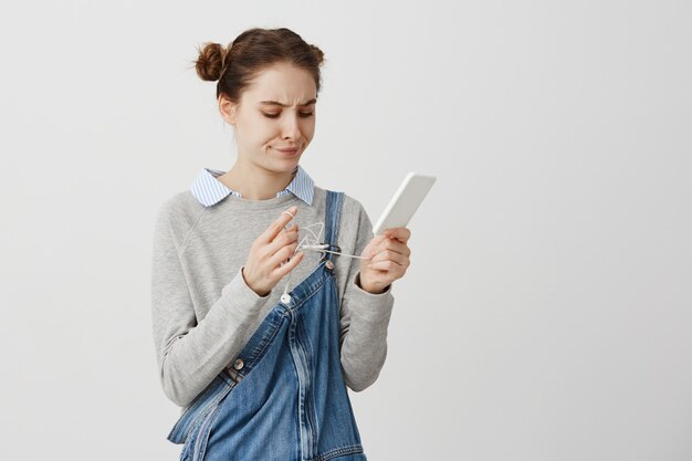 Bella ragazza adulta che si irrita mentre cerca di districare il filo dalle cuffie. La donna in smartphone casuale della tenuta con svela le cuffie che sono turbate. Reazioni umane