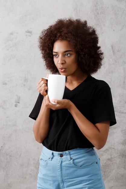 Bella ragazza africana che tiene tazza sopra la parete leggera.