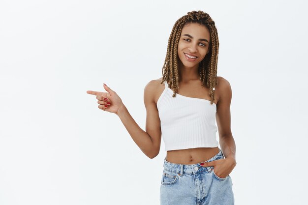 Bella ragazza afro-americana alla moda sorridente, dito puntato a sinistra al logo