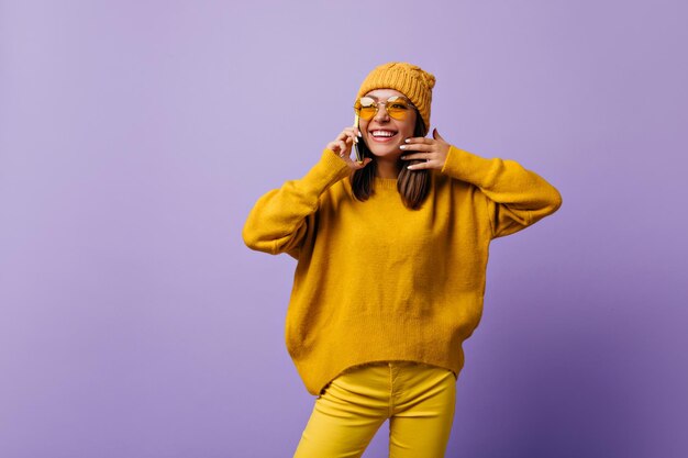 Bella ragazza allegra che ride durante la conversazione telefonica con la sua anima gemella Ritratto isolato di giovane bruna in pantaloni gialli luminosi