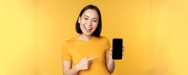 Bella ragazza asiatica felice che mostra l'applicazione dello schermo del telefono cellulare sul gadget dello smartphone in piedi dove
