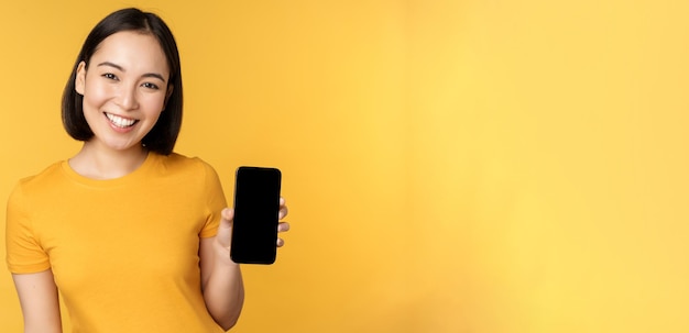 Bella ragazza asiatica felice che mostra l'applicazione dello schermo del telefono cellulare sul gadget dello smartphone in piedi dove