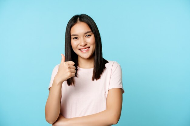 Bella ragazza asiatica sorridente che mostra pollice in su approva smth bene d'accordo nel raccomandare lo sta...