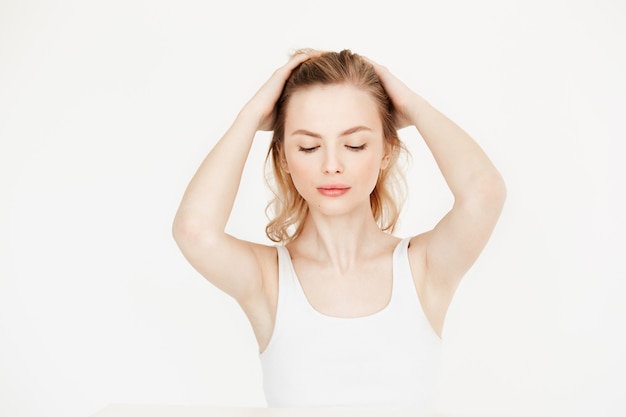 Bella ragazza bionda con pelle fresca pulita che si siede al tavolo toccando i capelli. Bellezza e spa per la cura della pelle. Occhi chiusi.