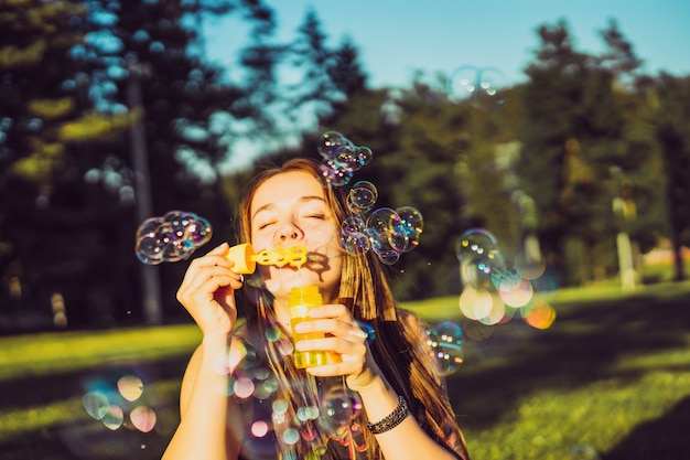 bella ragazza bruna con i capelli lunghi soffia bolle di sapone nel parco