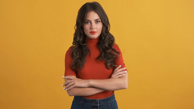 Bella ragazza bruna in cima rossa con le mani incrociate guardando con sicurezza a porte chiuse su sfondo colorato