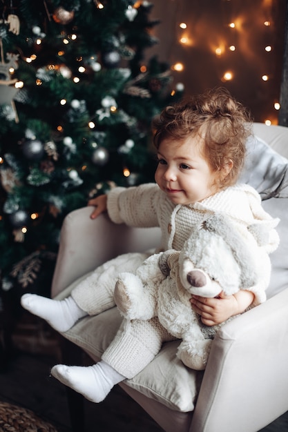 Bella ragazza caucasica con i capelli ricci si siede vicino a un grande bellissimo albero di Natale e si rilassa