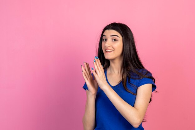 Bella ragazza che batte le mani e sta in piedi su sfondo rosa Foto di alta qualità