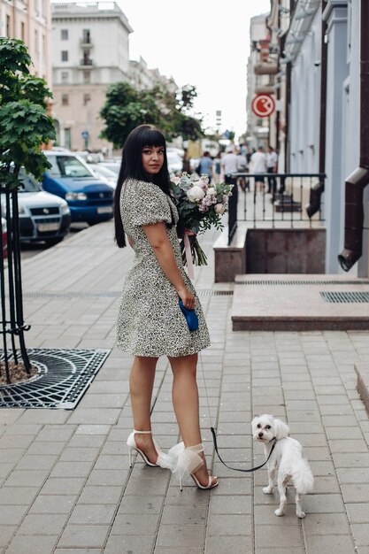 Bella ragazza che cammina con un cagnolino bianco sulla strada della città animali domestici all'aperto fem...