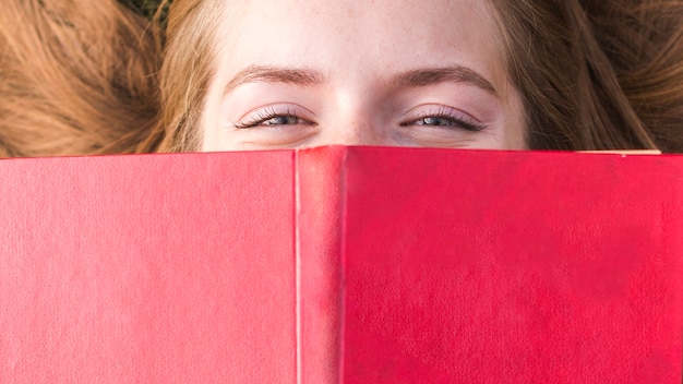 Bella ragazza che copre la bocca con un libro rosso