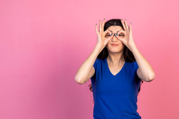 Bella ragazza che fa le mani come un binocolo e guarda la fotocamera Foto di alta qualità