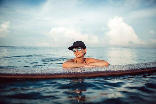 Bella ragazza che posa seduta su una tavola da surf nell&#39;oceano