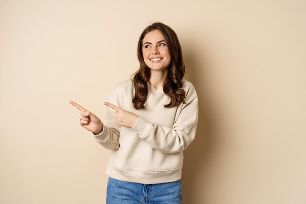 Bella ragazza che punta e guarda a sinistra ridendo e sorridendo felice mentre mostra il logo della pubblicità...