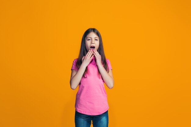 Bella ragazza che sembra sorpresa isolata sulla parete arancione