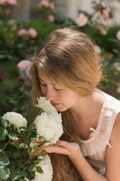 Bella ragazza che sente l'odore, che tiene i fiori in vestito rosa fuori durante il giorno.