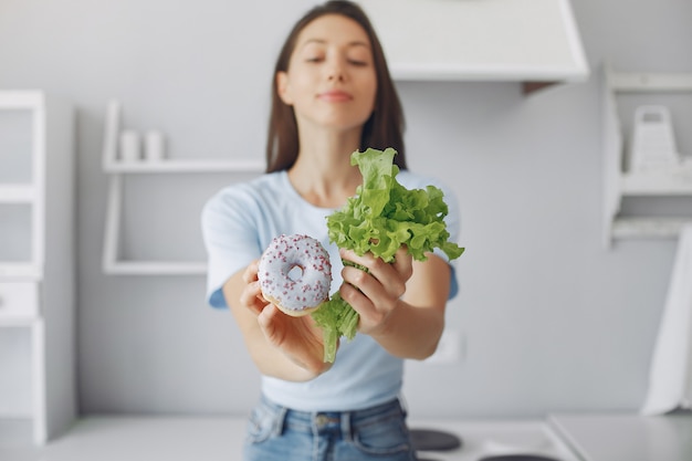 Bella ragazza che sta in una cucina con la ciambella e la foglia