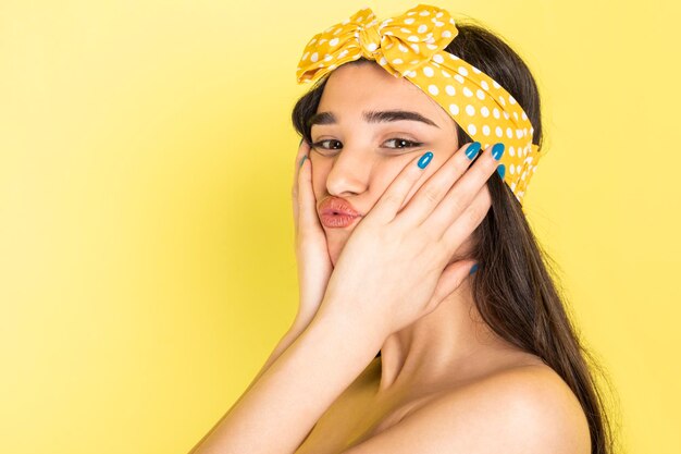 Bella ragazza che tiene le mani sul viso e in piedi su sfondo giallo Foto di alta qualità