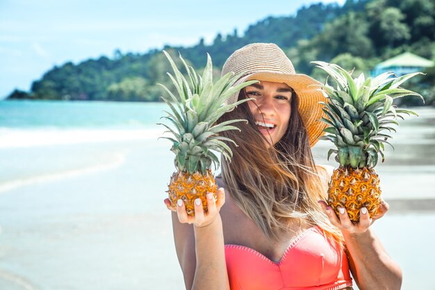 bella ragazza con ananas su una spiaggia esotica, uno stato d'animo felice e un bel sorriso, primo piano