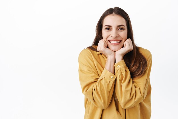 Bella ragazza con un bel sorriso, viso carino magro sulle mani e guardare qualcosa di adorabile, guardando con ammirazione e interesse, ascoltandoti, in piedi felice su sfondo bianco