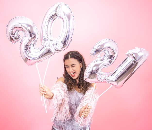 Bella ragazza con un sorriso in un vestito festivo su uno sfondo rosa studio tenendo palloncini d'argento per il concetto di nuovo anno