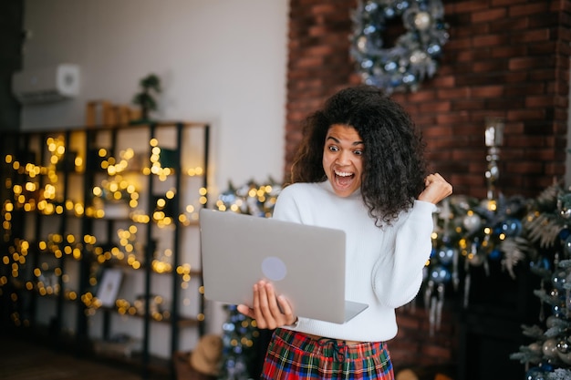 Bella ragazza dai capelli ondulati allegra allegra allegra allegra allegra e allegra che tiene in mano il raggiungimento dell'obiettivo del laptop