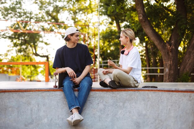Bella ragazza e giovane ragazzo che parlano felicemente mentre trascorrono del tempo insieme al moderno skatepark