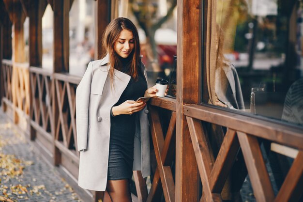 bella ragazza elegante in piedi nella città d&#39;autunno e bere un caffè