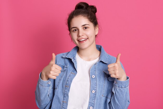 Bella ragazza felice che indossa abbigliamento elegante, mostrando il pollice in alto, esprimendo emozioni positive