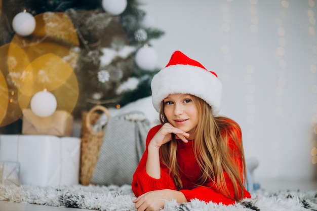 Bella ragazza in cappello della santa sotto l'albero di Natale