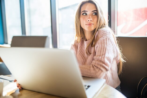 Bella ragazza in maglione bianco di moda a lavorare sul suo computer portatile nella caffetteria nel tempo quotidiano