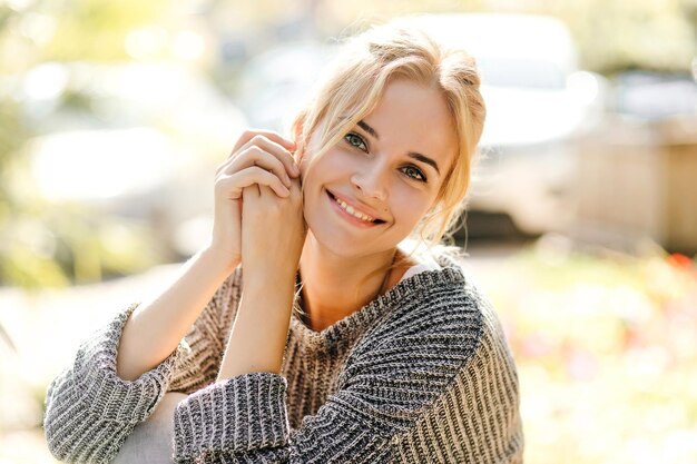 Bella ragazza in maglione oversize alla moda si chinò e guardava la fotocamera sullo sfondo delle auto con un sorriso