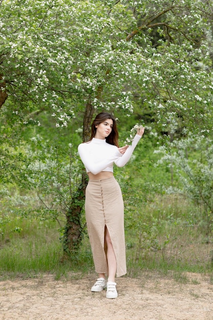 Bella ragazza in piedi nel parco fiorito che tiene il ramo di un albero in attesa di ammirare