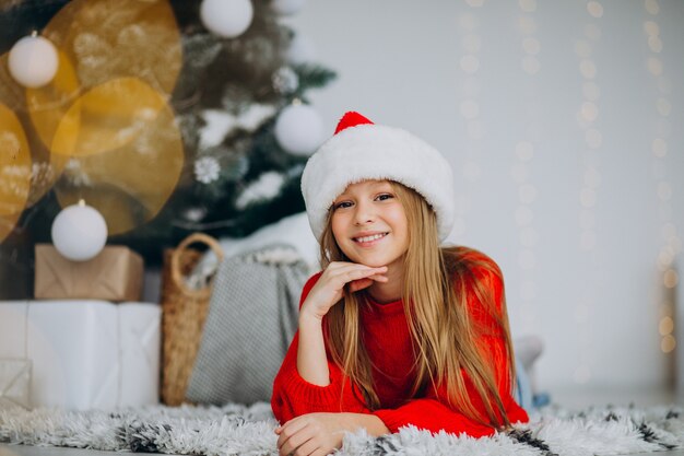 Bella ragazza in santa cappello sotto l'albero di Natale