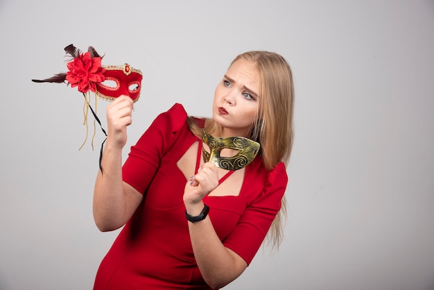 Bella ragazza in un vestito rosso che tiene le maschere di carnevale.