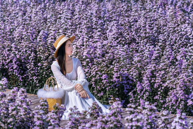 Bella ragazza in vestito bianco che si siede nei campi di fiori di Margaret