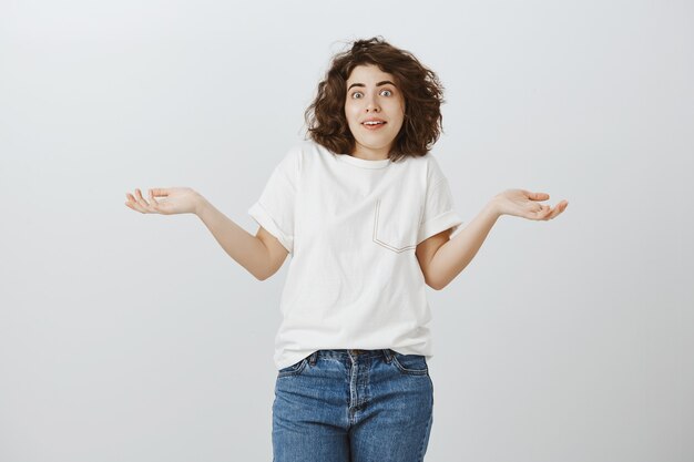 Bella ragazza incapace che scrolla le spalle con le mani aperte di lato, non so niente, non ne ho idea