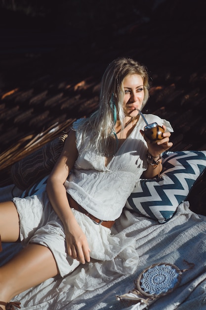 Bella ragazza indiana del hippie con capelli biondi lunghi sul tetto che beve il tè del compagno.