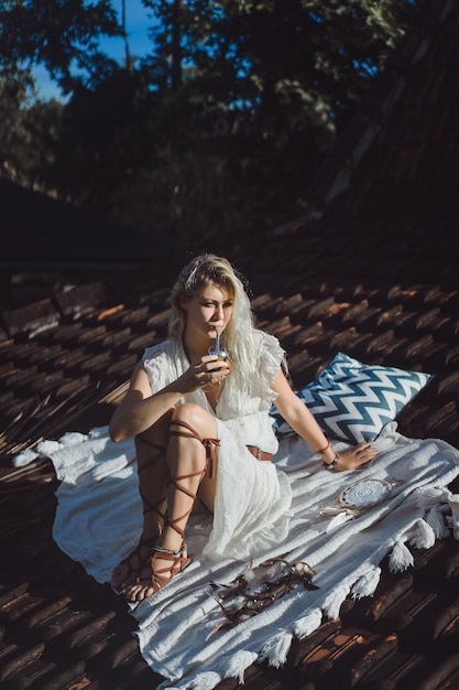 Bella ragazza indiana del hippie con capelli biondi lunghi sul tetto che beve il tè del compagno.