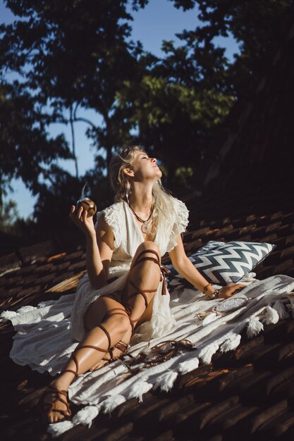 Bella ragazza indiana del hippie con capelli biondi lunghi sul tetto che beve il tè del compagno.