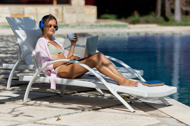 Bella ragazza lavora al computer vicino alla piscina