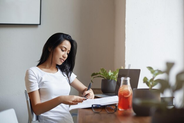 Bella ragazza mancina che studia nella caffetteria che prende le note i