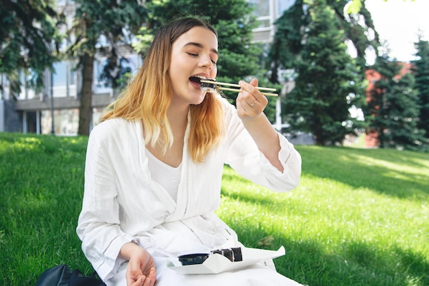 Bella ragazza mangia sushi seduto sull'erba nel parco