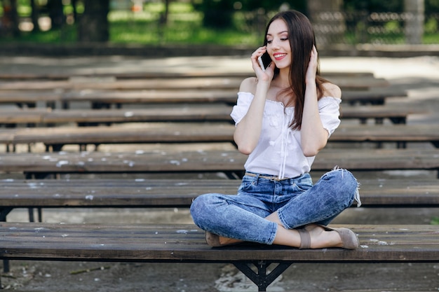 Bella ragazza parla al telefono seduto sulla panchina in un parco